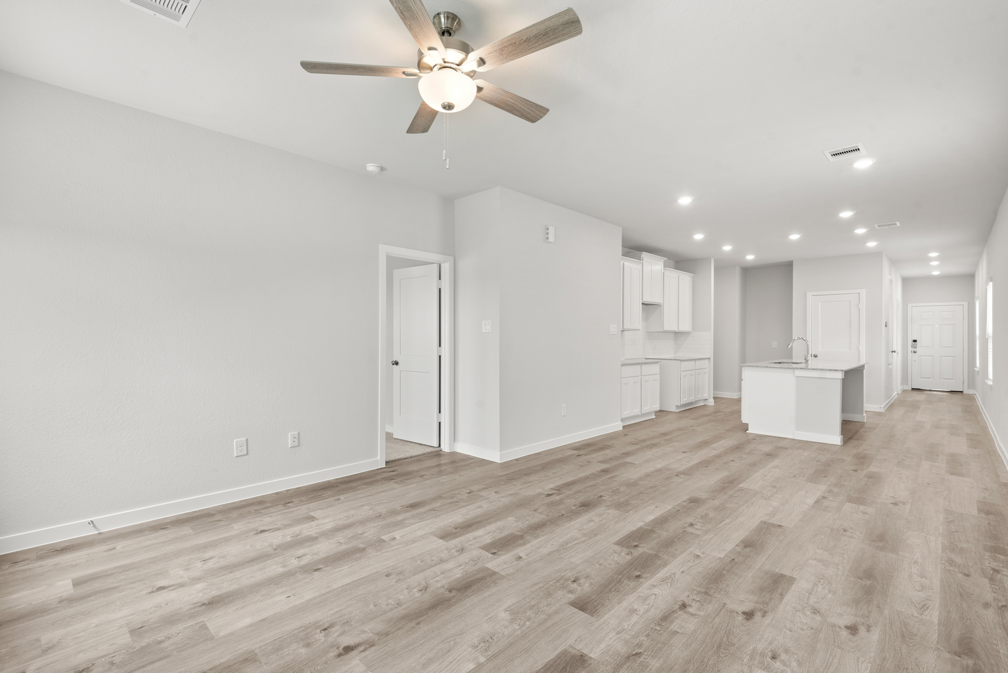 A large empty room with a ceiling fan and white cabinets.