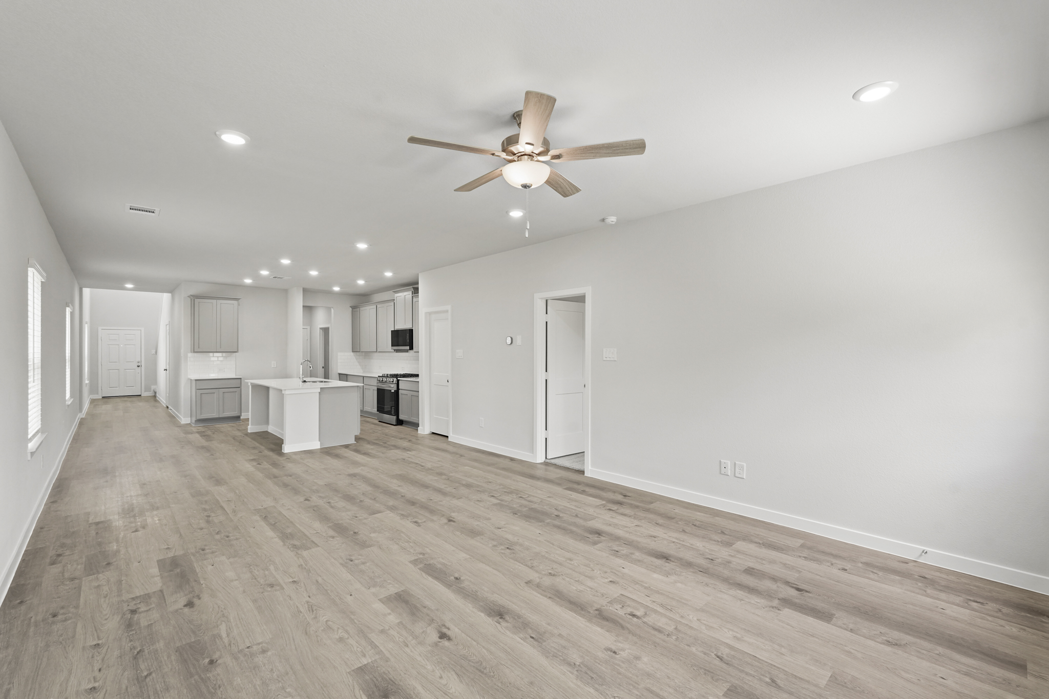 A large empty room with a ceiling fan and a wood floor.