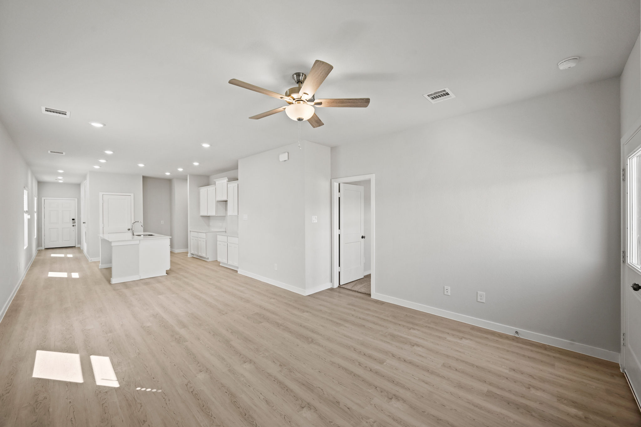 A large empty room with a ceiling fan and white cabinets.