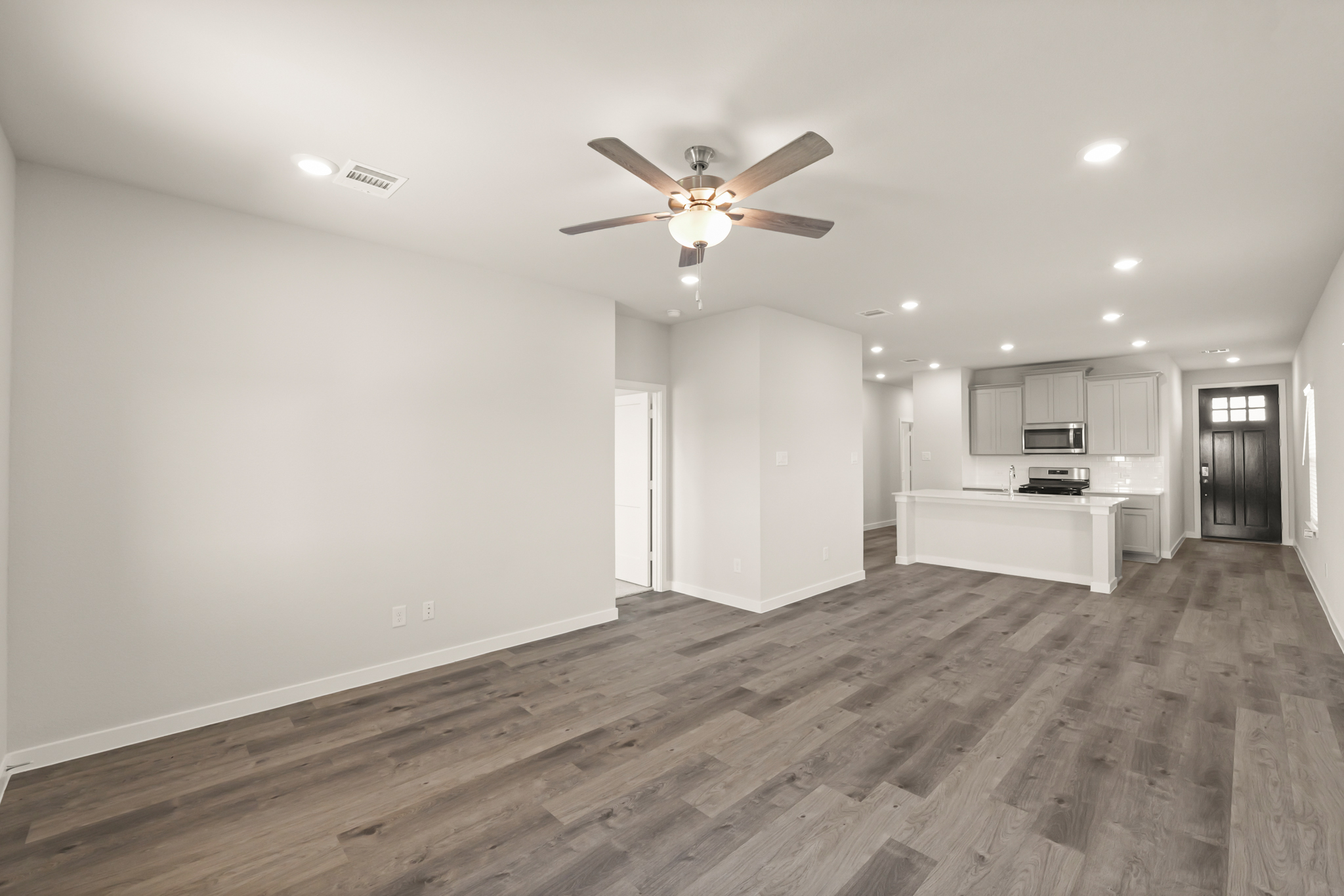 A large empty room with a ceiling fan and a wood floor.